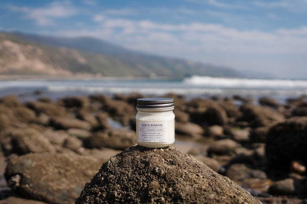 Handmade soy candle in mason jar seated on a mossy stone at Rincon Beach, Santa Barbara
